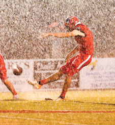 football player kicking the ball in the rain